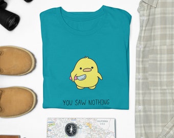 Puede incluir: Una camiseta azul turquesa con un pollito amarillo de dibujos animados sosteniendo un cuchillo. El texto "You Saw Nothing" está impreso debajo del pollito.