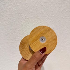Puede incluir: Dos tapas redondas de bamb&uacute; con un patr&oacute;n de vetas de madera claras. Una tapa se superpone ligeramente a la otra. Cada tapa tiene un peque&ntilde;o inserto de pl&aacute;stico blanco en el centro.