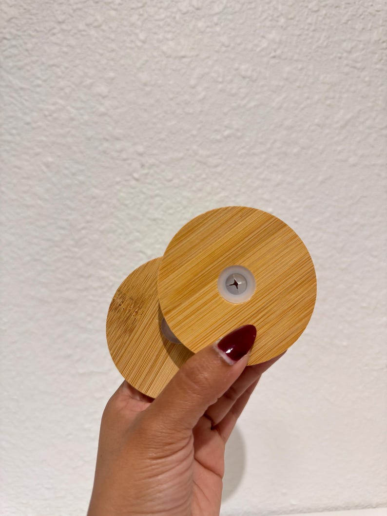 Puede incluir: Dos tapas redondas de bamb&uacute; con un patr&oacute;n de vetas de madera claras. Una tapa se superpone ligeramente a la otra. Cada tapa tiene un peque&ntilde;o inserto de pl&aacute;stico blanco en el centro.