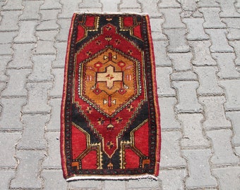 May include: A red, orange, and black patterned rug with a geometric design. The rug has a fringe border and is laid out on a gray concrete surface.