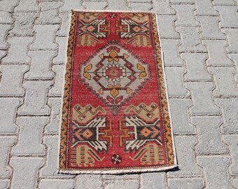 May include: A red, beige, and blue patterned rug with a geometric design. The rug has a fringe border and is made of wool.