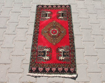 May include: A red runner rug with a traditional geometric pattern in brown, black, and green. The rug has a fringe border.