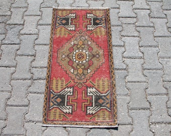 May include: A red, gold, and black patterned rug with a geometric design. The rug is approximately 2 feet long and 1 foot wide.