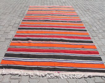 Pode incluir: Um tapete listrado com listras laranja, vermelho, preto, branco e azul. O tapete tem franjas na borda inferior.