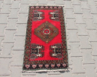 May include: A rectangular, hand-woven rug with a vibrant red field. The rug features a central brown medallion with a floral design, and geometric patterns in black, white, and green. The border is a dark brown with a repeating pattern.