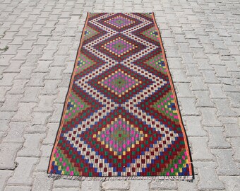 May include: A colourful geometric patterned rug with a red, green, blue, yellow, and white colour scheme. The rug has a diamond pattern with a fringe border.