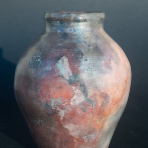 May include: A rustic, hand-thrown pottery vase with a mottled, multi-coloured glaze. The glaze features shades of brown, red, and grey, creating a unique and earthy look.
