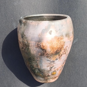 Puede incluir: Un jarrón de cerámica gris oscuro con un esmalte único y moteado. El esmalte tiene tonos de marrón, rosa y verde, creando un aspecto rústico y terroso.