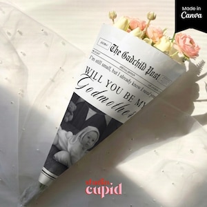 May include: A floral bouquet in a newspaper-style cone, featuring pink and cream blooms. The cone displays a baby photo and the text "WILL YOU BE MY Godmother". The bottom of the cone has the text "studio cupid".