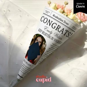 Op de afbeelding: Een boeket bloemen verpakt in een kegelvormige krant met de tekst "CONGRATS! Emily Wilson KEEP BELIEVING IN YOURSELF". Het toont een foto van een afgestudeerde en bevat roze en gele bloemen. Het woord "cupid" staat onderaan.