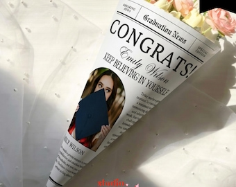 May include: A bouquet of flowers wrapped in a newspaper-style cone. The newspaper reads "CONGRATS! Emily Wilson KEEP BELIEVING IN YOURSELF" with a photo of a graduate. The bouquet includes pink and yellow flowers. The bottom of the cone has the word "cupid".