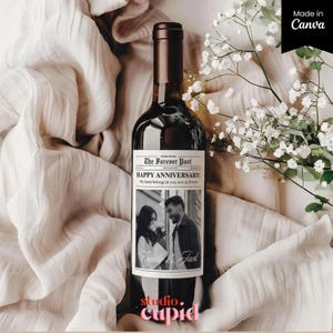 May include: A dark wine bottle with a custom label that reads "The Forever Post HAPPY ANNIVERSARY!" with a black and white photo of a couple. The bottle is set against a backdrop of soft, beige fabric and white flowers.