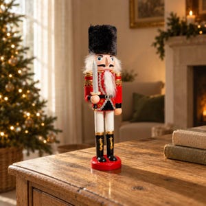 May include: A wooden nutcracker figurine dressed in a red jacket with gold trim, white trousers, and black boots. The figure wears a tall black fuzzy hat, has a white beard, and holds a silver-colored sword in its right hand while standing on a red base.