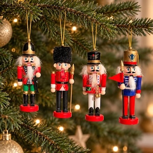Könnte beinhalten: Vier hängende Nussknacker-Ornamente mit goldenen Schnüren, jedes mit einer einzigartigen Uniform in Rot, Blau, Schwarz und Weiß, bemalten Gesichtsdetails, weißen Kunstfellbärten und runden roten Sockeln, aufgehängt an grünen Tannenzweigen.