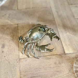 Op de afbeelding: Een zilverkleurig krabbeeldje met gedetailleerde klauwen en een getextureerde schaal.