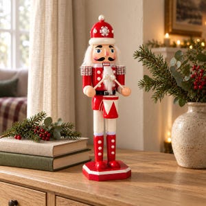 Puede incluir: Una figura de cascanueces de madera vestida con un uniforme rojo y blanco con un sombrero a juego. La figura tiene una barba blanca, sostiene dos baquetas y está de pie detrás de un pequeño tambor rojo y blanco. Decorada con perlas blancas.