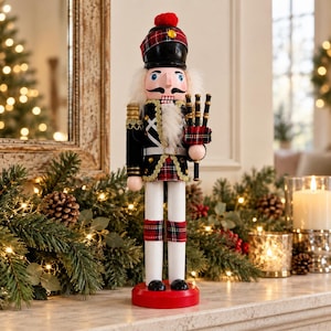 May include: A nutcracker figurine dressed in a black and red tartan uniform with gold trim. The figure wears a black hat with a red pom-pom, features a white beard, and holds a set of black bagpipes. It stands on a round red base.