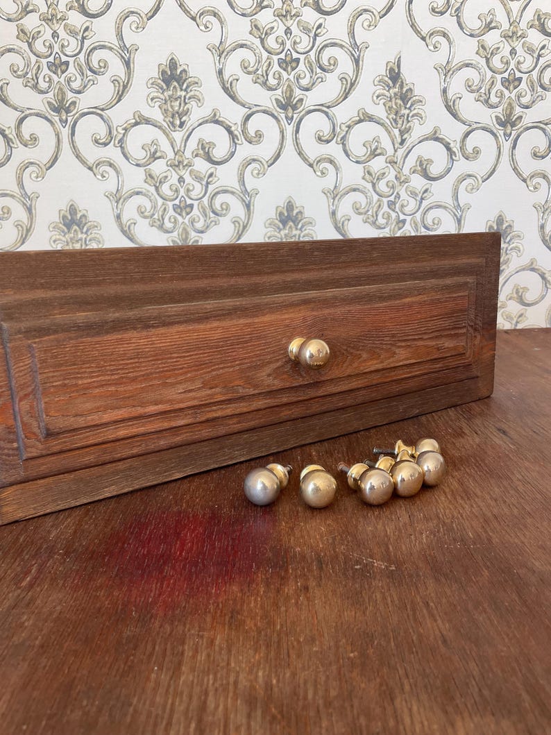 May include: A wooden cabinet door with two brass knobs and a set of six brass knobs. The cabinet door is a dark brown color with a rectangular design. The knobs are round and shiny.