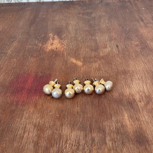 May include: A collection of seven small, round cabinet knobs. Each knob has a silver-colored, spherical body and a gold-colored base. The knobs are arranged on a wooden surface with a warm, brown tone.