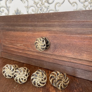Op de afbeelding: Een set van zes antieke messing kastknoppen met een spiraalvormig ontwerp. De knoppen worden weergegeven op een houten oppervlak, met twee knoppen bevestigd aan een donkerbruine houten lade. De knoppen hebben een vintage, sierlijke uitstraling.