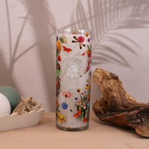 May include: A clear glass candle holder with a white background and colorful floral and butterfly designs. The candle holder is decorated with the words 
