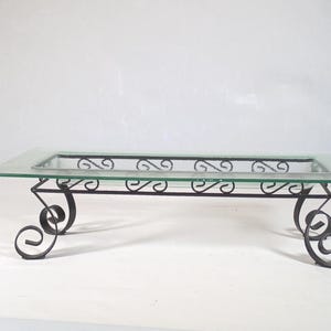 May include: A rectangular glass tray with a clear, flat surface and a recessed center, supported by a black metal stand featuring decorative scrollwork legs and a matching black metal frame that outlines the glass insert.