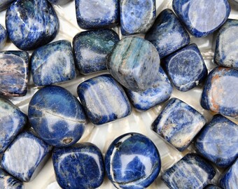 May include: A collection of tumbled blue and white lapis lazuli stones. The stones are smooth and polished, with a variety of patterns and textures.