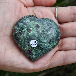 May include: Green heart-shaped stone with red flecks. The stone has a white sticker with the number 23 on it.