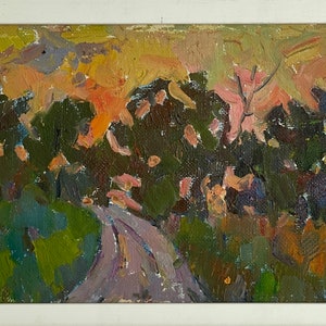 May include: An oil painting in a white frame depicts a landscape scene. The artwork features a road leading through a forest with green and brown foliage. The sky is a mix of orange and yellow hues, suggesting a sunset or sunrise.