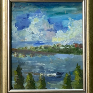 May include: Oil painting of a landscape scene with a river reflecting a cloudy sky. The artwork features a gold-colored frame and a palette of blues, greens, and white. The painting depicts trees, water, and a distant shoreline.