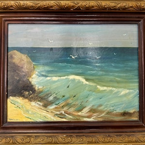 May include: A framed oil painting depicting a seascape with a rocky shore, crashing waves, and seagulls flying overhead. The painting has a blue, green, and white color scheme.