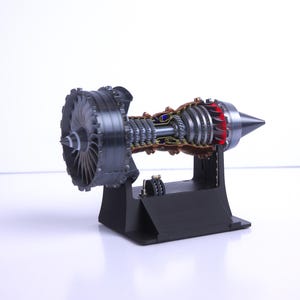 May include: A detailed cutaway model of a jet engine, showing the internal components and workings. The engine is mounted on a black stand and has a silver and black finish.