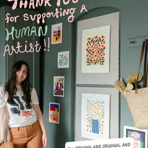 May include: A woman stands in front of a wall adorned with original art prints. The prints feature floral and abstract designs in various sizes and colors. Text above reads "Thank You for supporting a Human Artist!!" and "All designs are original and hand drawn by me, Haley."