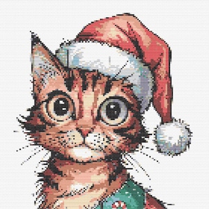 Op de afbeelding: Kruissteekontwerp van een kat met een kerstmuts en kerstoutfit. De kat heeft grote ogen en zit rechtop. De outfit is rood en groen met kerstversieringen.