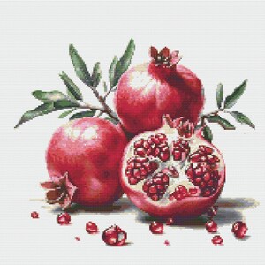 May include: A cross-stitch pattern featuring two whole red pomegranates and one halved pomegranate showing deep red seeds. Green leaves are attached to the stems. Several loose pomegranate seeds are scattered at the base of the fruit.