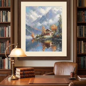 May include: A framed landscape painting featuring a cabin on a lakeshore with mountains in the background, displayed on a wall above a wooden desk with a lamp, books, and a leather chair. The artwork uses blue, green, and orange tones.