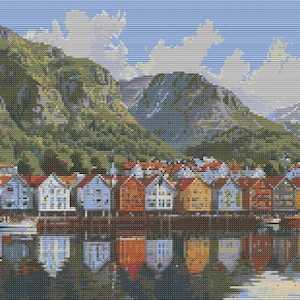 Op de afbeelding: Een kleurrijke rij huizen geschilderd in rood, blauw, geel en groen staat aan een waterkant met een bergketen op de achtergrond. De huizen worden weerspiegeld in het water.