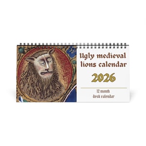 May include: A desk calendar with a medieval lion illustration. The calendar is titled "Ugly medieval lions calendar 2026" and is a 12-month desk calendar. The lion illustration is set against a red and gold background. The calendar is spiral-bound.