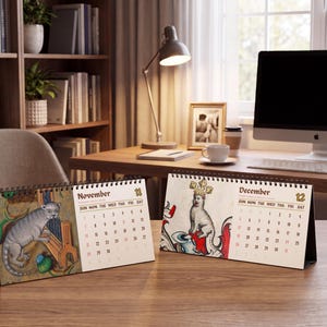 May include: Two spiral-bound desk calendars featuring medieval-style illustrations. The left calendar shows November with a grey creature playing a musical instrument. The right calendar shows December with a crowned creature and the text December 12.
