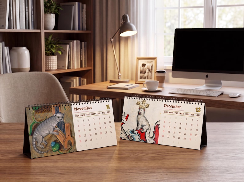 May include: Two spiral-bound desk calendars featuring medieval-style illustrations. The left calendar shows November with a grey creature playing a musical instrument. The right calendar shows December with a crowned creature and the text December 12.