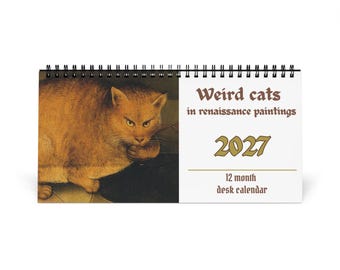 May include: A 2027 12-month desk calendar with a black spiral binding. The cover features an orange cat on the left and the text "Weird cats in renaissance paintings 2027 12 month desk calendar" printed in brown and gold on a white background.