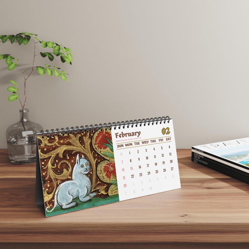 May include: A desk calendar for the month of February featuring a spiral binding at the top. The left side displays an illustration of a white cat against a dark gold and red floral background. The right side shows the calendar grid with the text February.