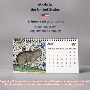 May include: A spiral-bound desk calendar featuring a medieval-style illustration of a cat on the left page and the month of July with a grid of dates on the right. The text includes the month name July, the number 07, and days of the week.