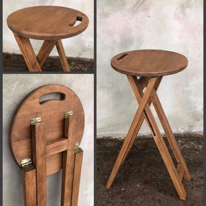 May include: A round wooden folding table with a handle on the top. The table is made of dark brown wood and has a natural finish. The legs fold up for easy storage.