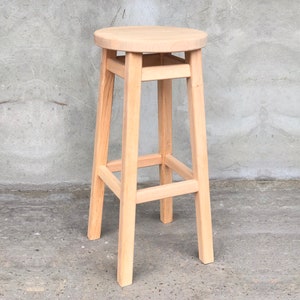 Op de afbeelding: Een barstoel van naturel hout met een ronde zitting en een eenvoudig, stevig ontwerp.
