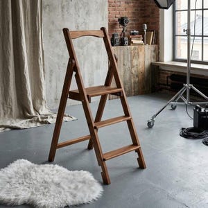 May include: A folding wooden step ladder with a warm brown finish, featuring three horizontal steps and a tall, arched top handle. The ladder is constructed with sturdy side rails and metal hinges that allow it to fold for storage.