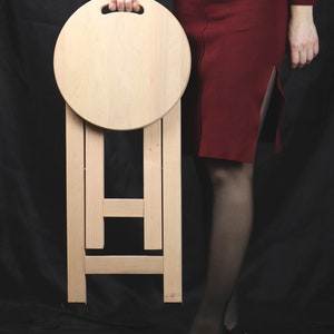 Taburete de madera plegable, ligero y portátil, con asiento redondo y asa cómoda. Asiento compacto y artesanal para espacios de vida modernos. Elegante y compacto.