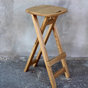 May include: A wooden folding bar stool with a natural finish. The stool has a simple, modern design and is made of solid wood.