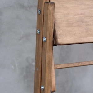 K&ouml;nnte beinhalten: Ein Klappstuhl aus Holz mit brauner Beize. Der Stuhl hat eine R&uuml;ckenlehne und eine Sitzfl&auml;che aus Latten. Der Stuhl ist aus massivem Holz gefertigt und hat eine robuste Konstruktion.