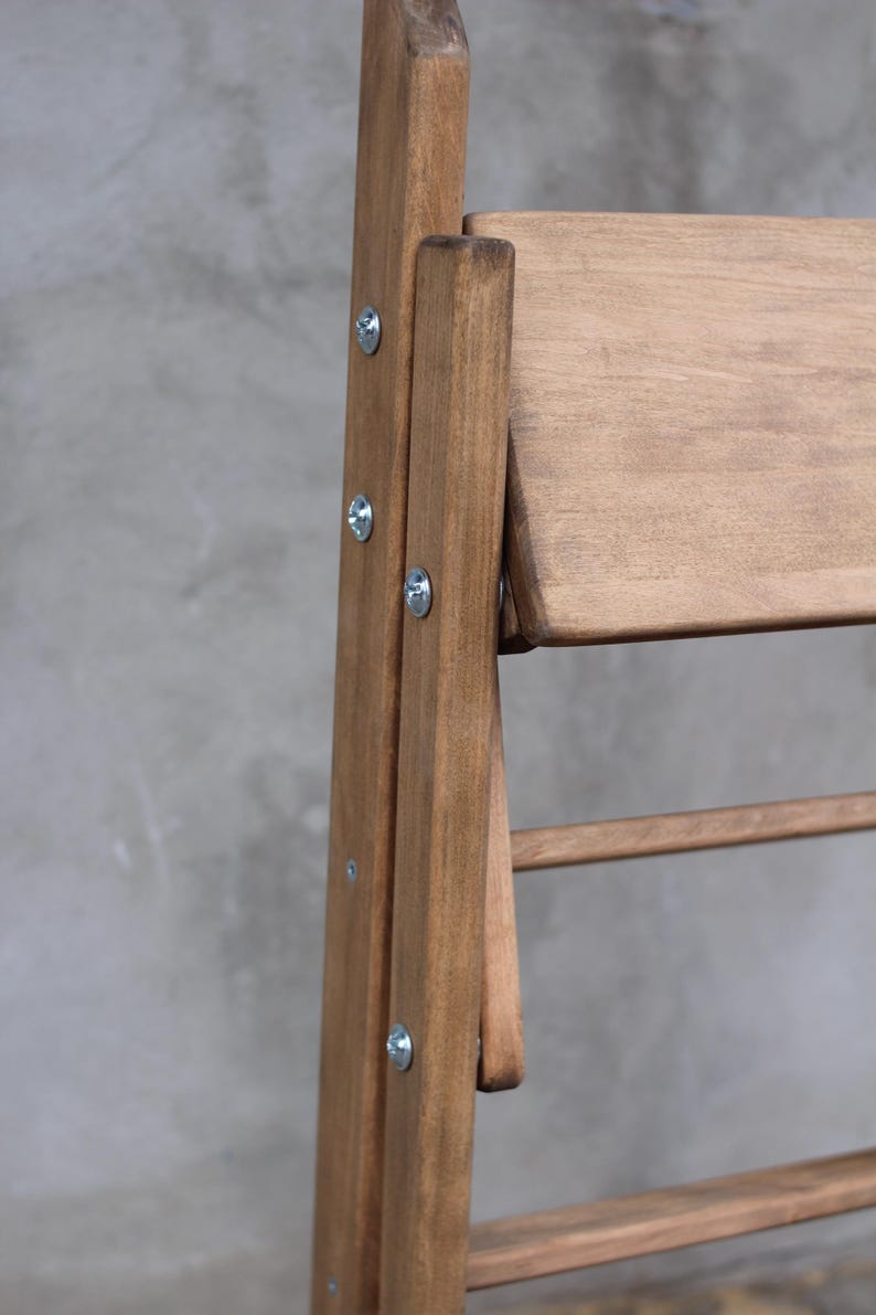 K&ouml;nnte beinhalten: Ein Klappstuhl aus Holz mit brauner Beize. Der Stuhl hat eine R&uuml;ckenlehne und eine Sitzfl&auml;che aus Latten. Der Stuhl ist aus massivem Holz gefertigt und hat eine robuste Konstruktion.